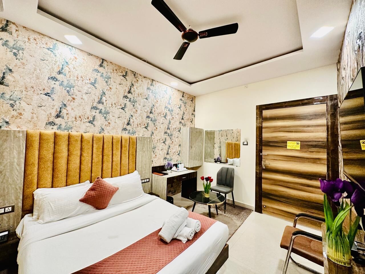 A hotel room with a bed, a desk, a chair, a mirror, and a door.