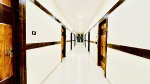 Um corredor comprido e estreito, com paredes brancas e detalhes em madeira, que leva a uma porta no final.