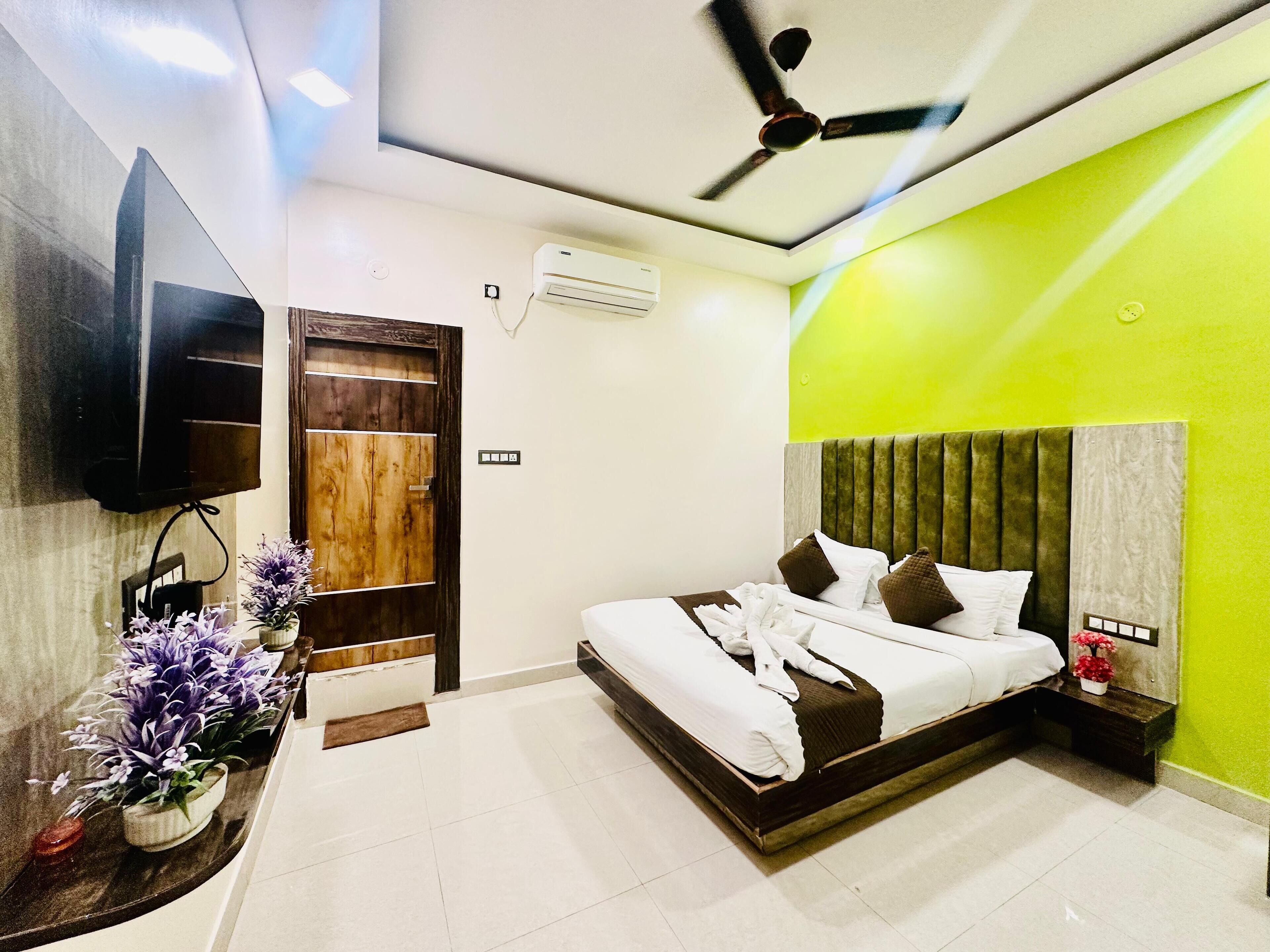 Una habitación de hotel moderna con una cama, un ventilador de techo, un televisor montado en la pared y una puerta de madera.