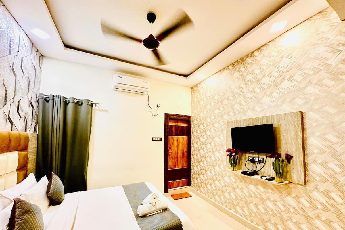 Een moderne hotelkamer met een bed, een plafondventilator, een airconditioning en een aan de muur bevestigde televisie, plus een decoratief wandpaneel.