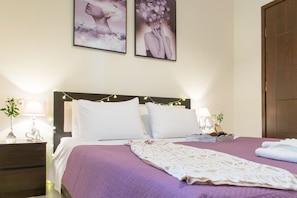 Un letto rifatto con una coperta viola e cuscini bianchi, un comodino con una lampada e due quadri appesi alla parete.