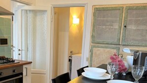 A compact kitchen with a dining table set for two, a stove, and a door leading to a bathroom.