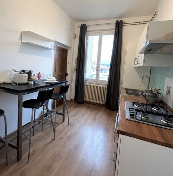A compact kitchen with a dining area, a stove, and a view through a window with curtains.