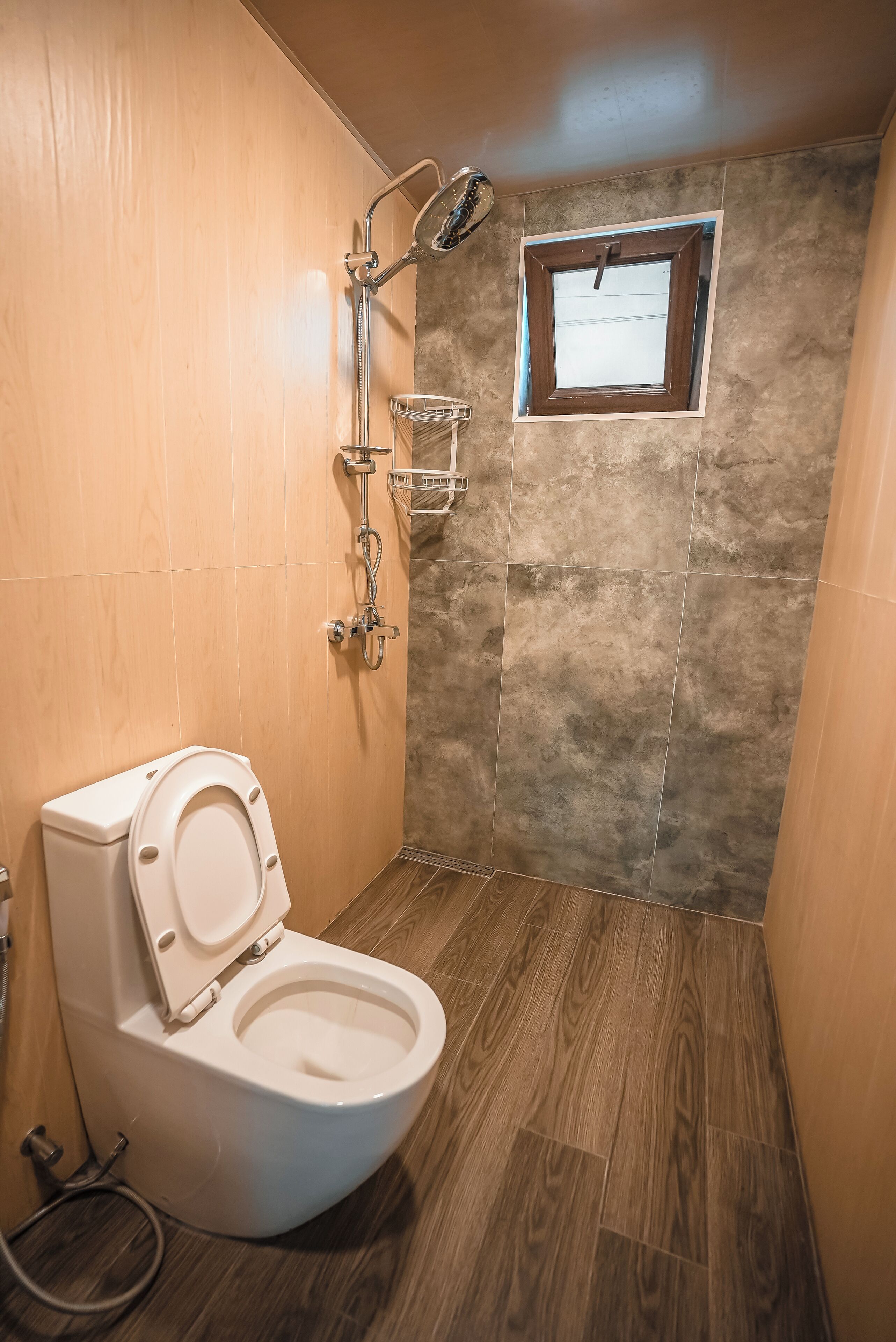 Ein Badezimmer mit Holzboden, einer weißen Toilette, einer Dusche mit Glastrennwand und einem kleinen Fenster.