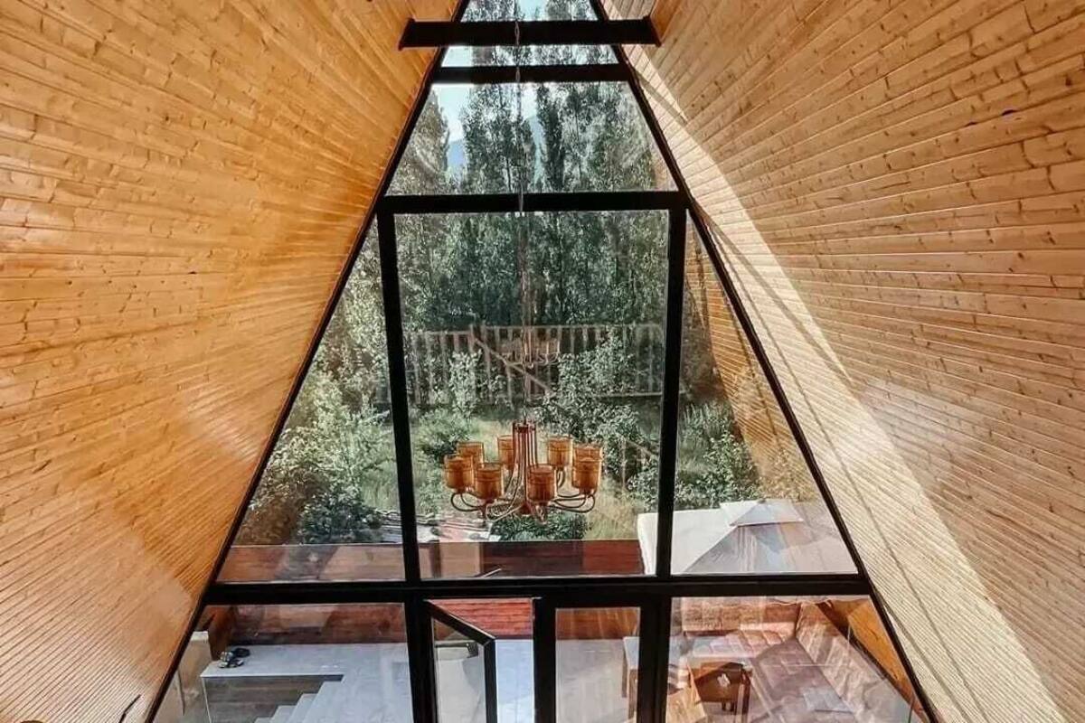 A triangular wooden interior with a glass ceiling, a wooden staircase, and a cushioned seating area.