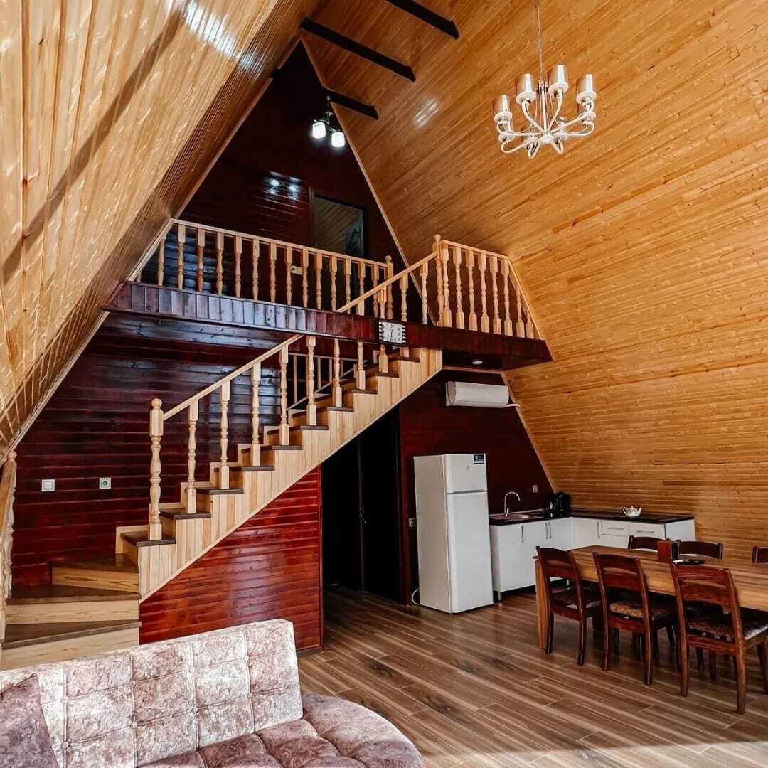 Un intérieur en bois avec un escalier menant à un niveau supérieur, un coin repas avec une table et des chaises, et un lustre.