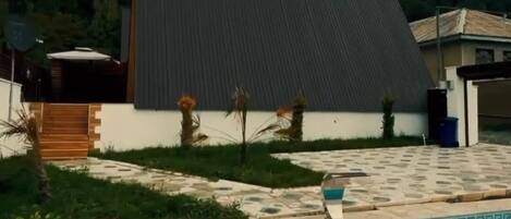 A modern building with a large sloped roof, a swimming pool with a decorative edge, and a paved patio area.