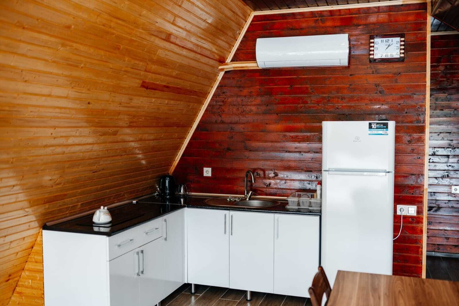 A compact kitchen with white cabinets, a black countertop, a sink, a refrigerator, and a clock on the wall.