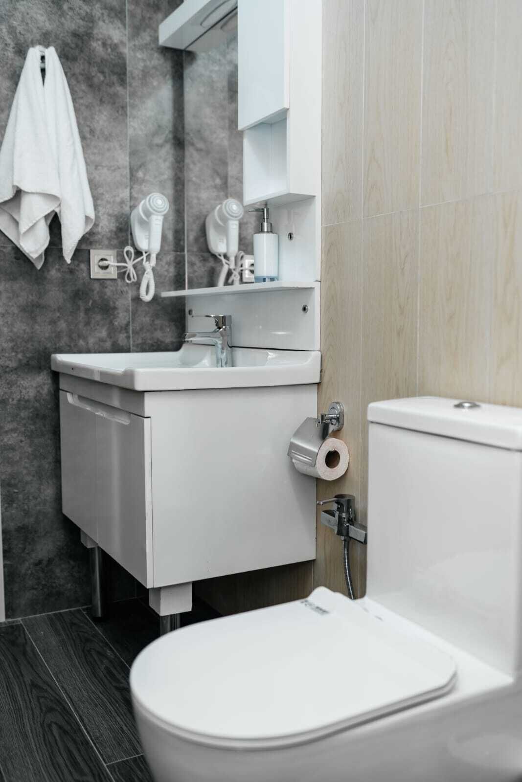 A modern bathroom with a white sink, a toilet, and a towel hanging on the wall.