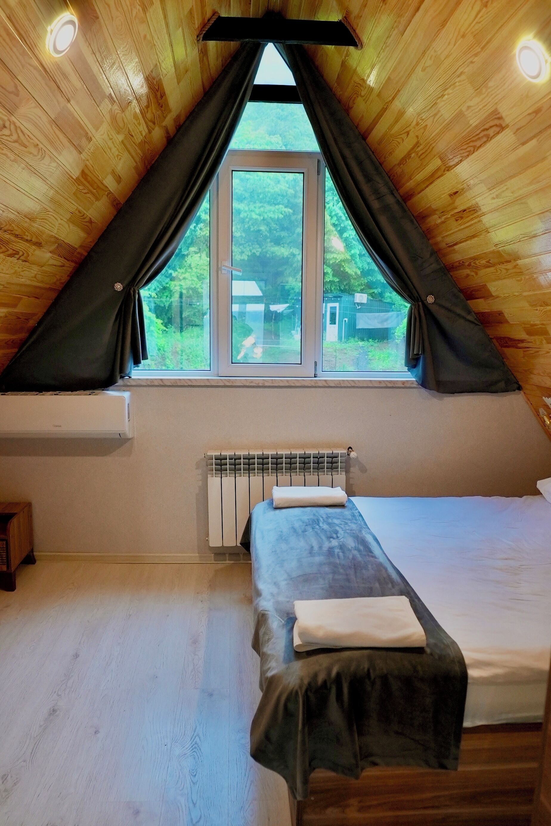 Et lille, hyggeligt rum med skråvægge, en enkeltseng, et vindue med gardiner og en radiator.
