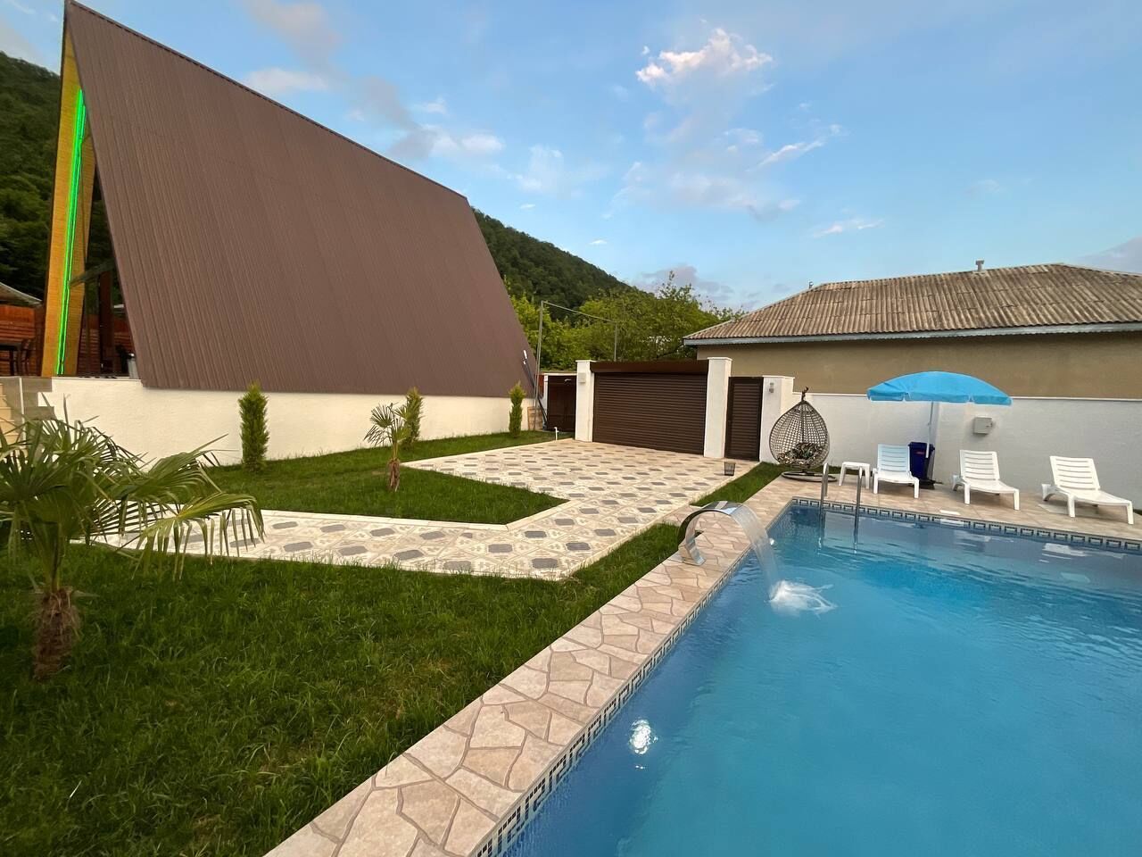 Una piscina con borde de piedra, zona de césped y un edificio con tejado inclinado.