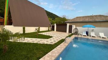 Una piscina con borde de piedra, zona de césped y un edificio con tejado inclinado.