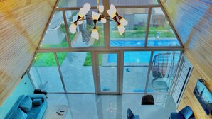A modern interior with a glass ceiling, a blue sofa, a dining table, and a view of a swimming pool. - 3Gozel Qabala (Gabala)
