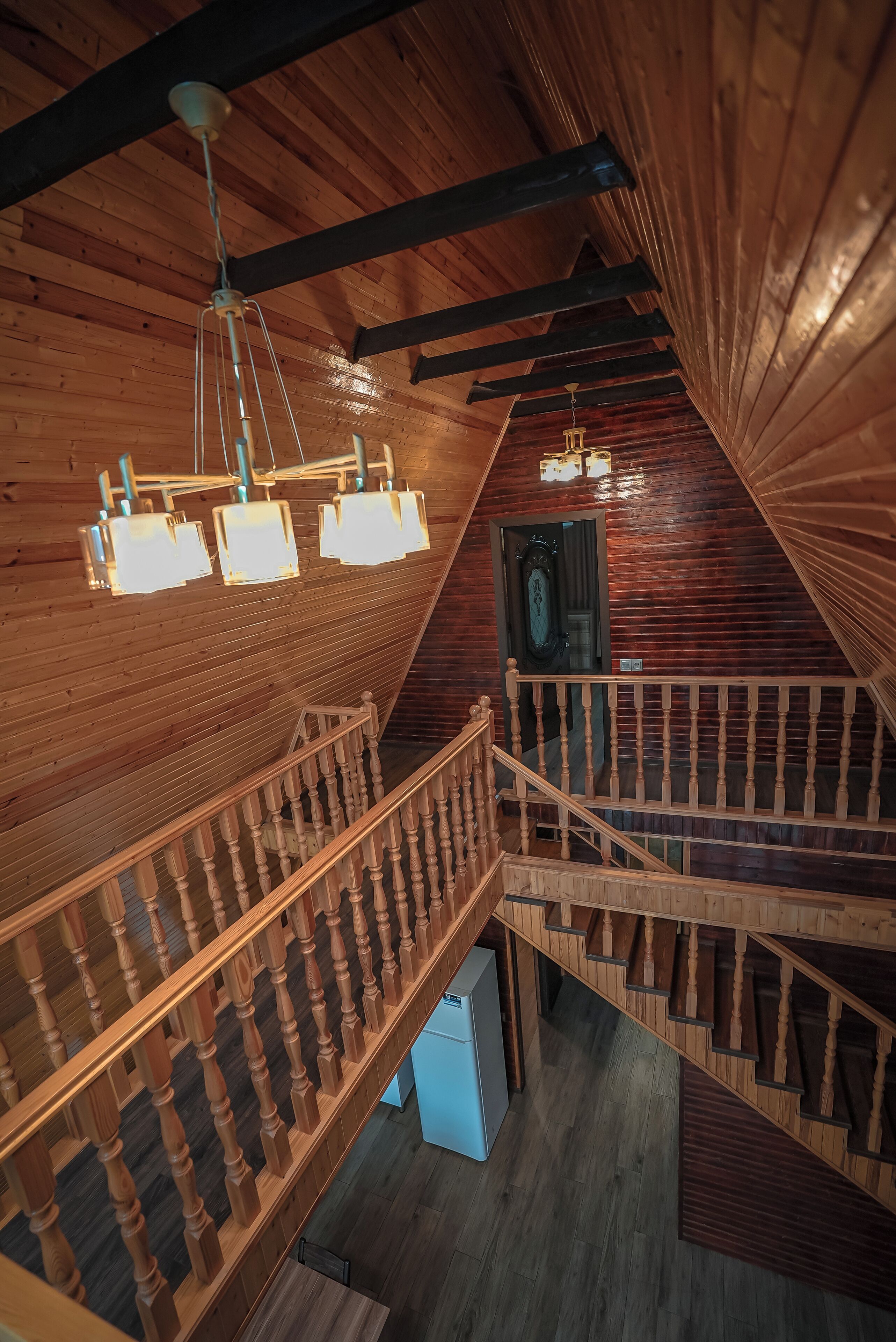 A wooden interior with a staircase, wooden beams, and hanging light fixtures.