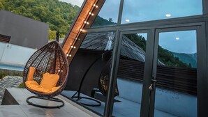 A modern outdoor seating area with a hanging chair and a glass enclosure with a view of a green hillside. - 3Gozel Qabala (Gabala)