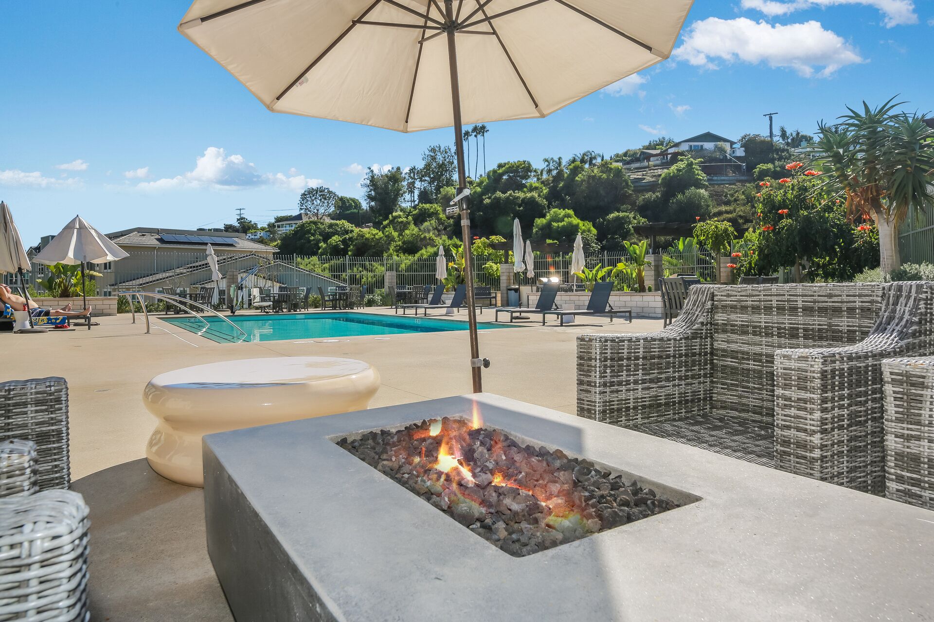 A poolside area with lounge chairs, a fire pit, and an umbrella.