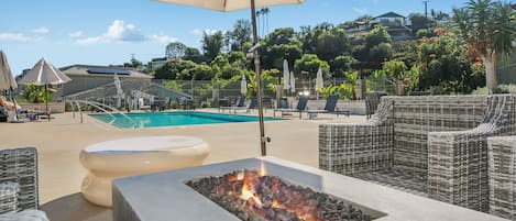 Uma área à beira da piscina com espreguiçadeiras, lareira e guarda-sol.