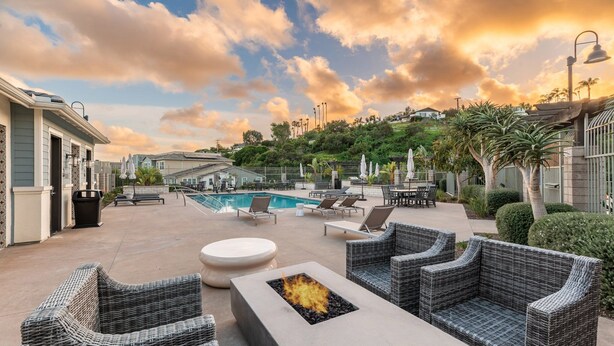 A poolside area with wicker furniture, a fire pit, and a view of the pool and surrounding greenery. - Spring Special 15% Off a Luxury Townhome with Pool & A/C (Oceanside)