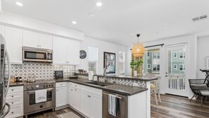 A modern kitchen with white cabinets, a stainless steel stove, and a large island with a sink. - Spring Special 15% Off a Luxury Townhome with Pool & A/C (Oceanside)