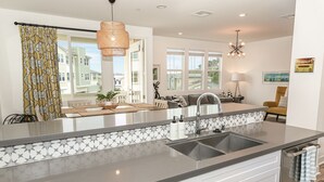 A modern kitchen with a large island, stainless steel appliances, and a view of the neighborhood. - Spring Special 15% Off a Luxury Townhome with Pool & A/C (Oceanside)