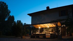 Un área de comedor al aire libre techada, con una mesa lista para dos personas, rodeada de macetas con plantas.