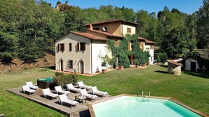 Una villa con piscina, mobiliario de exterior y abundante vegetación.