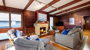 Una sala acogedora con chimenea, vigas de madera, televisor y asientos cómodos.