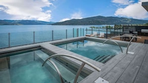 A pool area with clear water, a wooden deck, and a view of a lake and mountains.