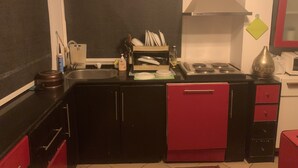 Une cuisine compacte aux couleurs rouge et noir, comprenant un évier, une cuisinière et un égouttoir à vaisselle.