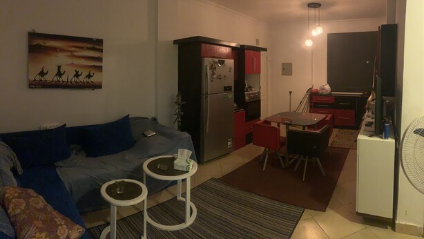 Un espace de vie compact comprenant un canapé, une petite table à manger, un réfrigérateur et un ventilateur.