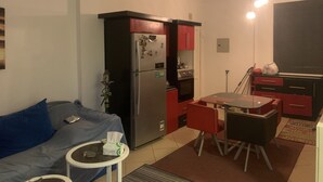 Un espace de vie compact comprenant un coin cuisine, un coin repas avec une table et des chaises, et un canapé avec une petite table d’appoint.