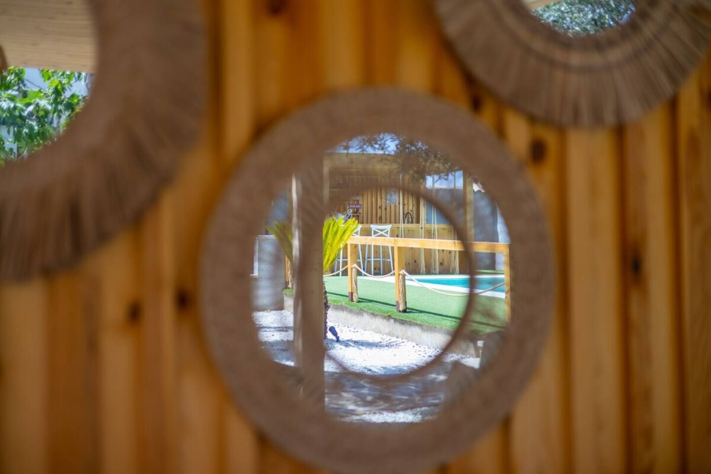 A circular window with a view of a wooden structure and a green area outside.
