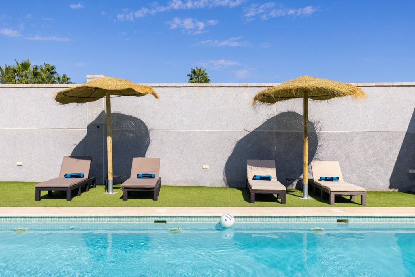 A swimming pool with two sun loungers and two thatched umbrellas.