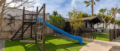A playground with a slide, climbing structure, and artificial grass.