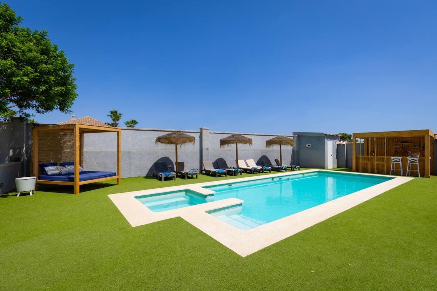 A swimming pool with lounge chairs and a wooden pergola.