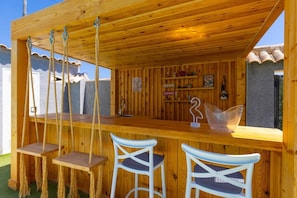 A wooden outdoor bar area with a counter, two bar stools, and a hanging rope swing. - WaterWheel Villa by Fidalsa (Almoradí)