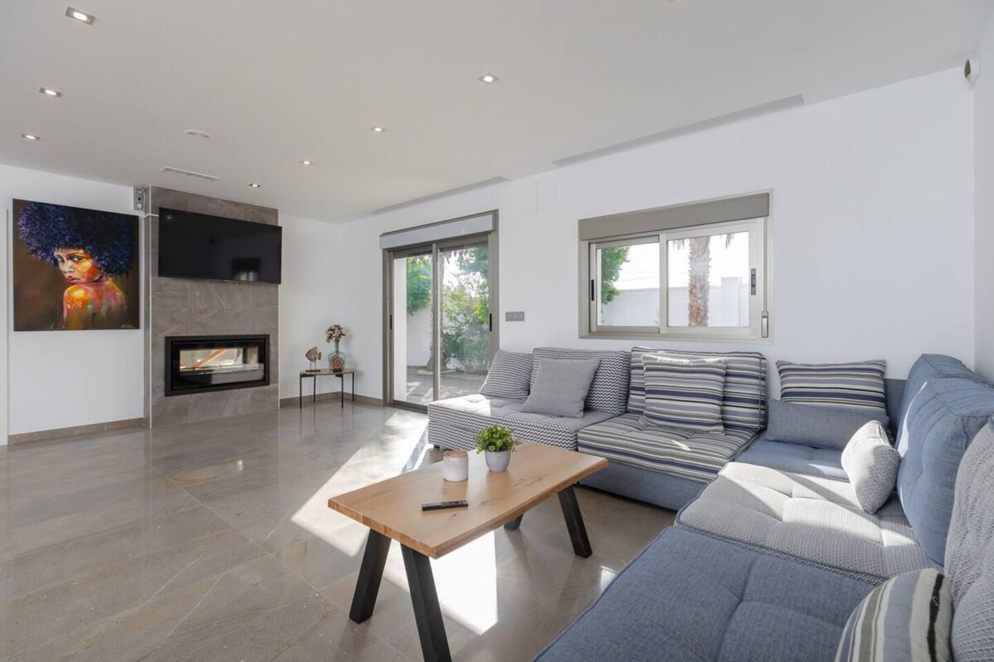 A modern living room with a sofa, a coffee table, a fireplace, and a large window.