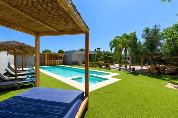 Ein Poolbereich mit Kunstgrasanlage, Liegestühlen und einer Holz-Pergola.