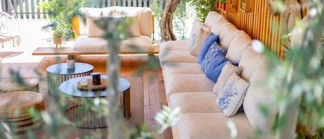 A cozy outdoor seating area with a cushioned sofa, round tables, and a wooden deck.