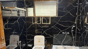 Un baño con paredes de mármol negro, inodoro blanco, bañera y zona de ducha.