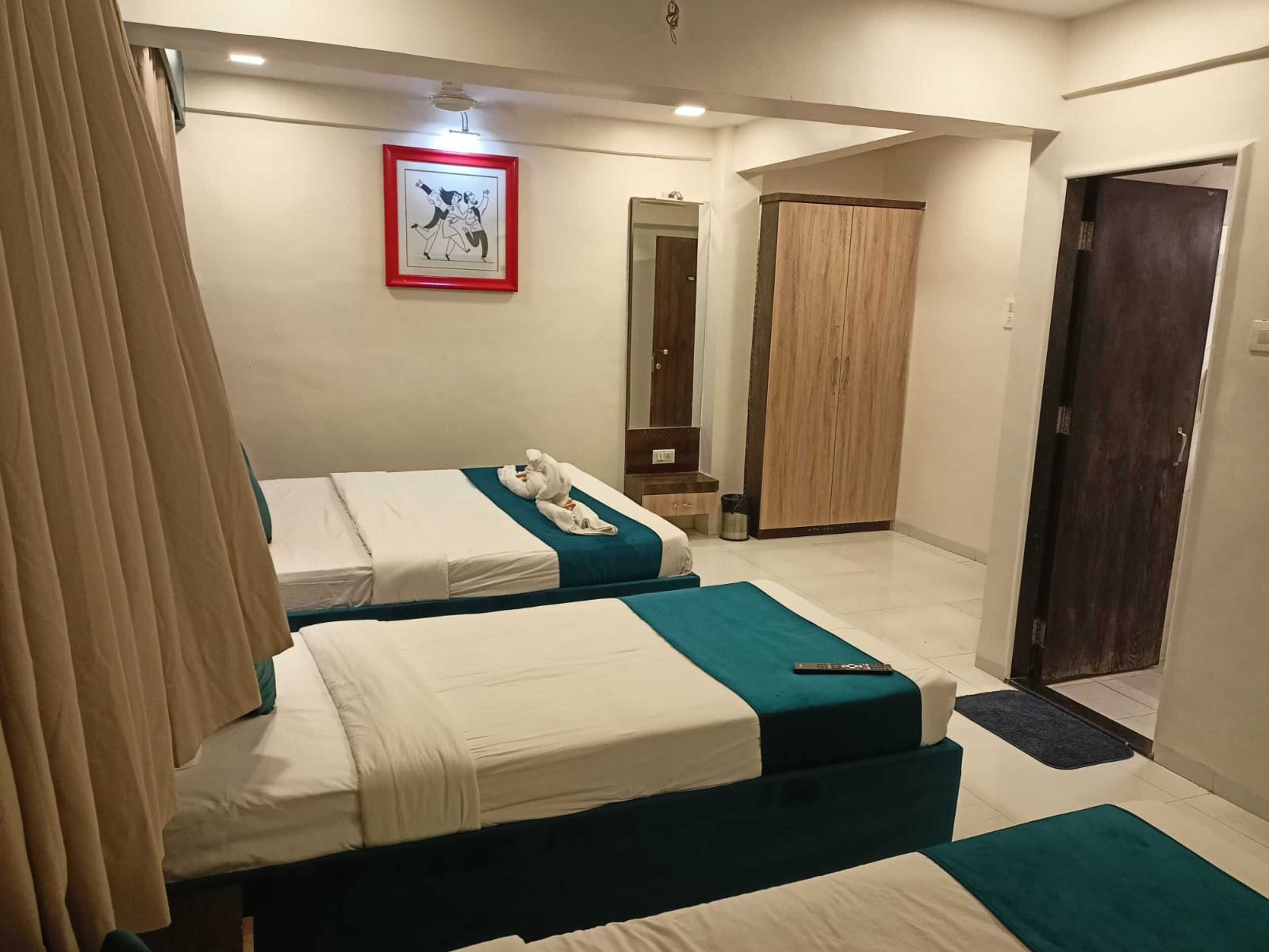 A hotel room with two beds, a wooden wardrobe, a mirror, and a framed picture on the wall.