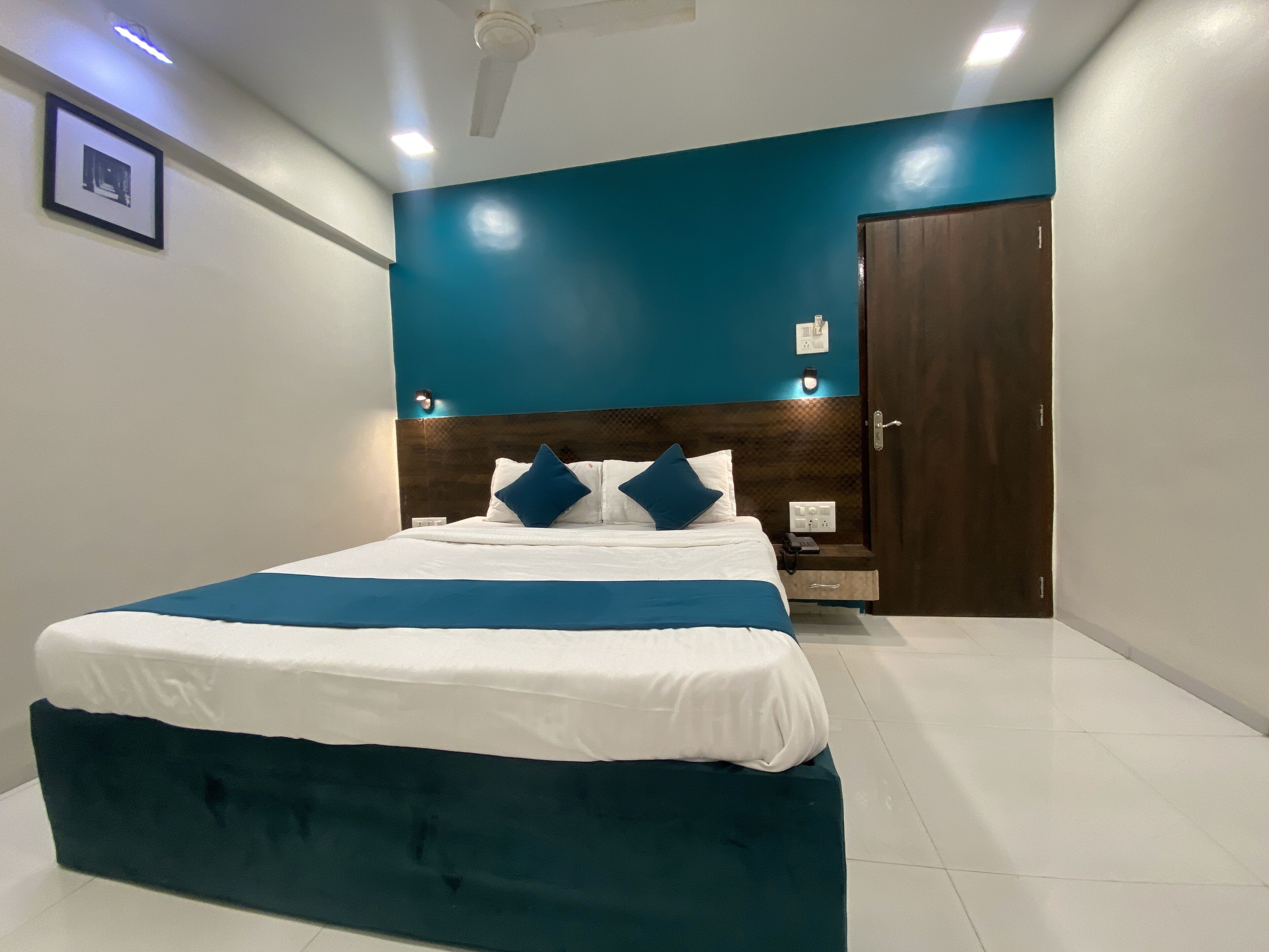 A modern bedroom with a large bed, a nightstand, a wooden door, and a ceiling fan.