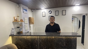 Un mostrador de recepción con encimera de mármol, una cámara de seguridad instalada en la pared, un certificado enmarco y un estante pequeño con un objeto decorativo.