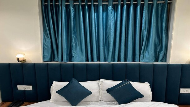 Una cama con cabecera oscura, ropa de cama blanca y dos almohadas oscuras.