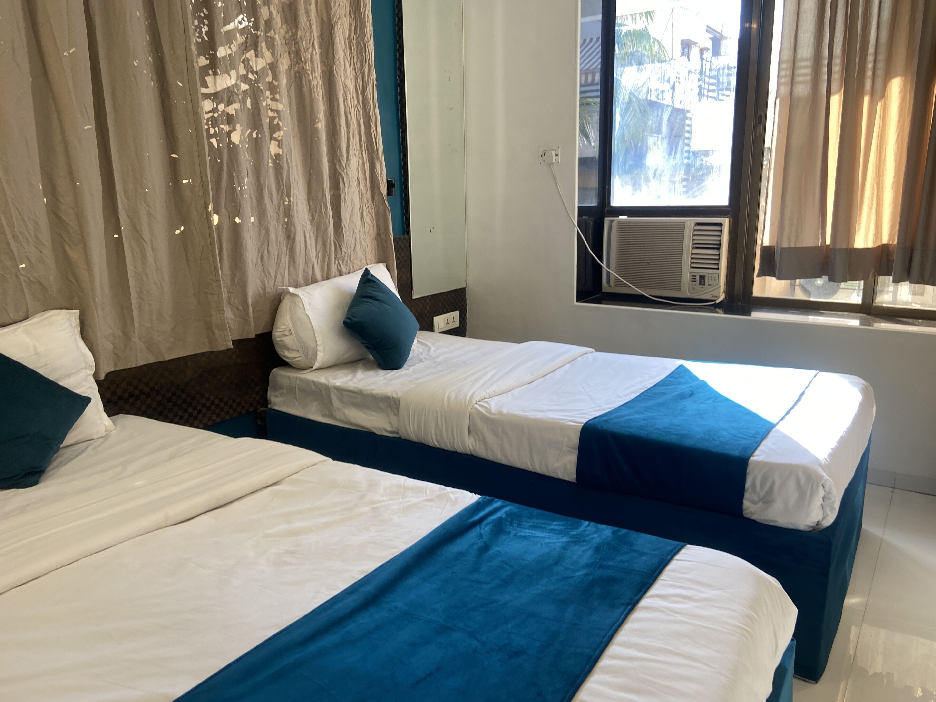 A hotel room with two beds, a window with an air conditioner, and curtains.