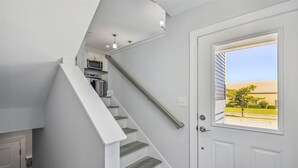 A staircase with a handrail leading to a kitchen area with appliances. - Bayside Bliss 205, Newly Constructed single family house in Uptown Ocean City (Ocean City)