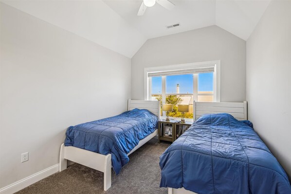 A bedroom with two single beds, a window with a view of a lighthouse, and a ceiling fan.