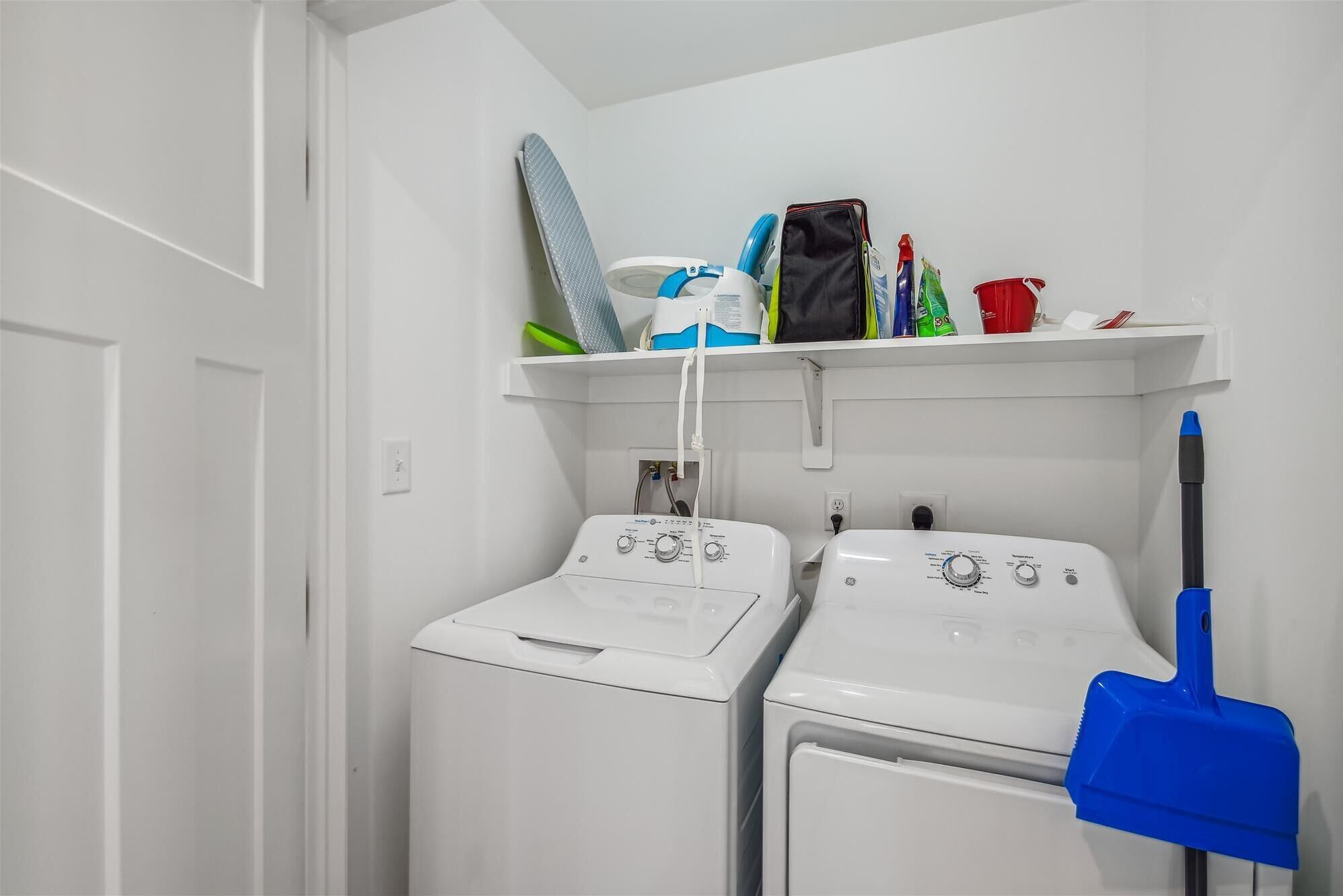 Une buanderie avec deux machines à laver blanches, une serpillière bleue et divers produits de nettoyage rangés sur une étagère.