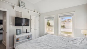 A bedroom with a bed, a TV mounted on the wall, a desk with a computer, and a window with blinds. - Bayside Bliss 205, Newly Constructed single family house in Uptown Ocean City (Ocean City)
