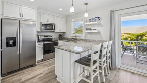 A modern kitchen with white cabinets, stainless steel appliances, a granite countertop, and a dining area with white chairs. - Bayside Bliss 205, Newly Constructed single family house in Uptown Ocean City (Ocean City)